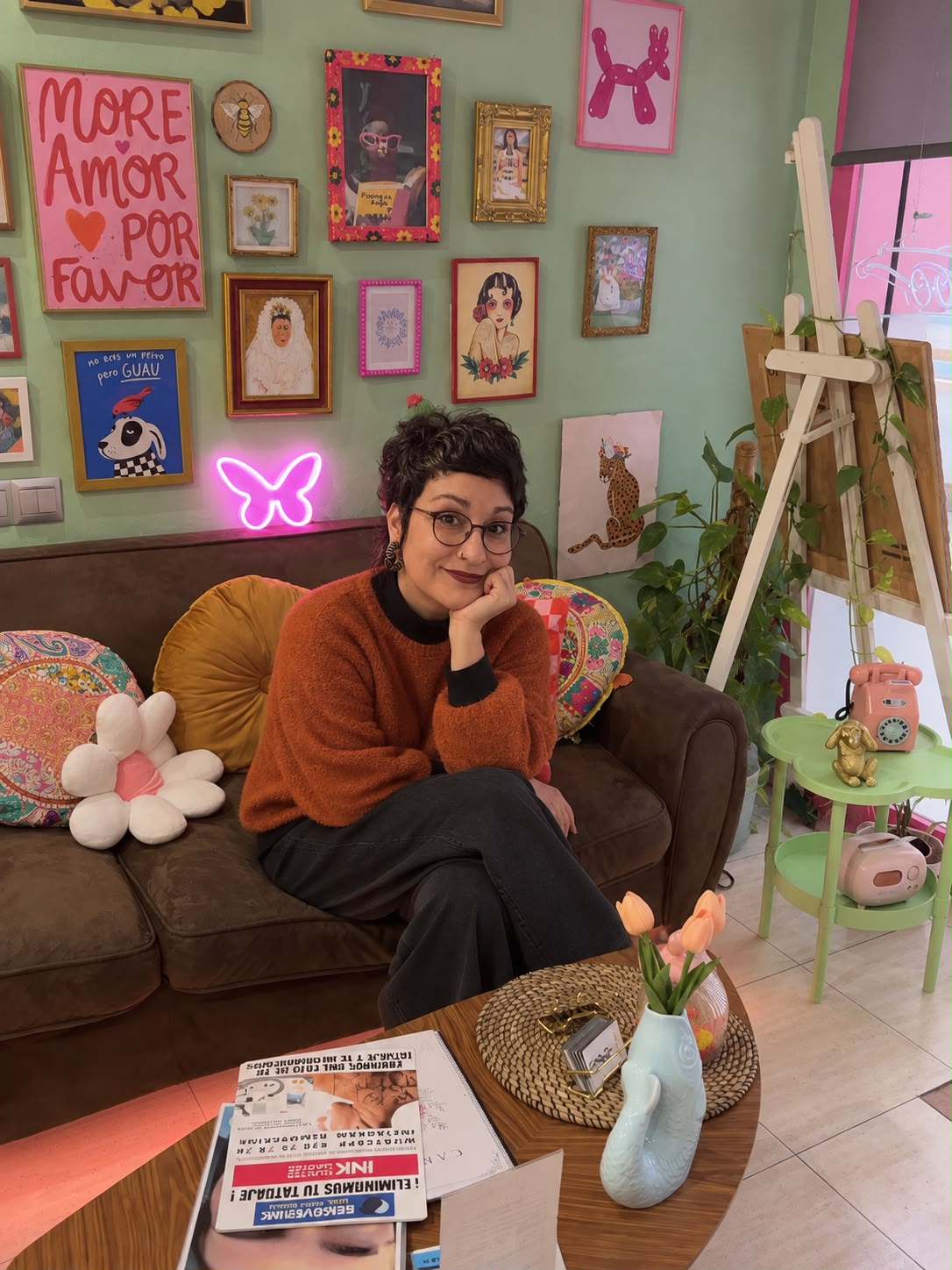 Palmira sentada en el sofá de la sala de espera del estudio, delante de la pared de cuadros